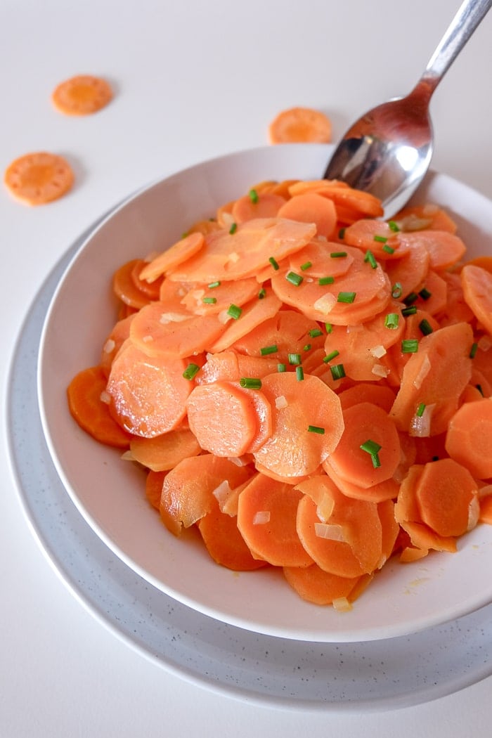 sliced carrots in bowl on plate with silver spoon