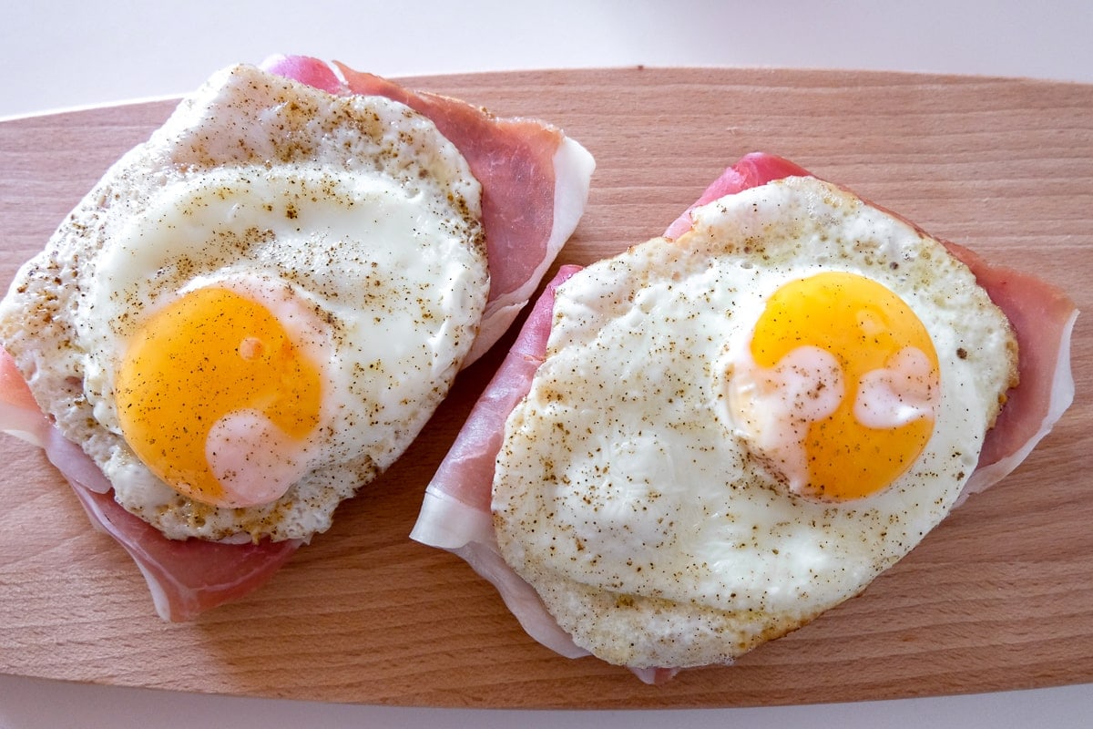 two fried eggs on bread on wooden cutting board