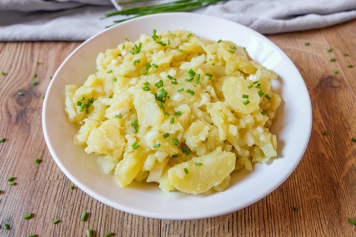 white bowl of yellow potato salad on wood with green chopped chives
