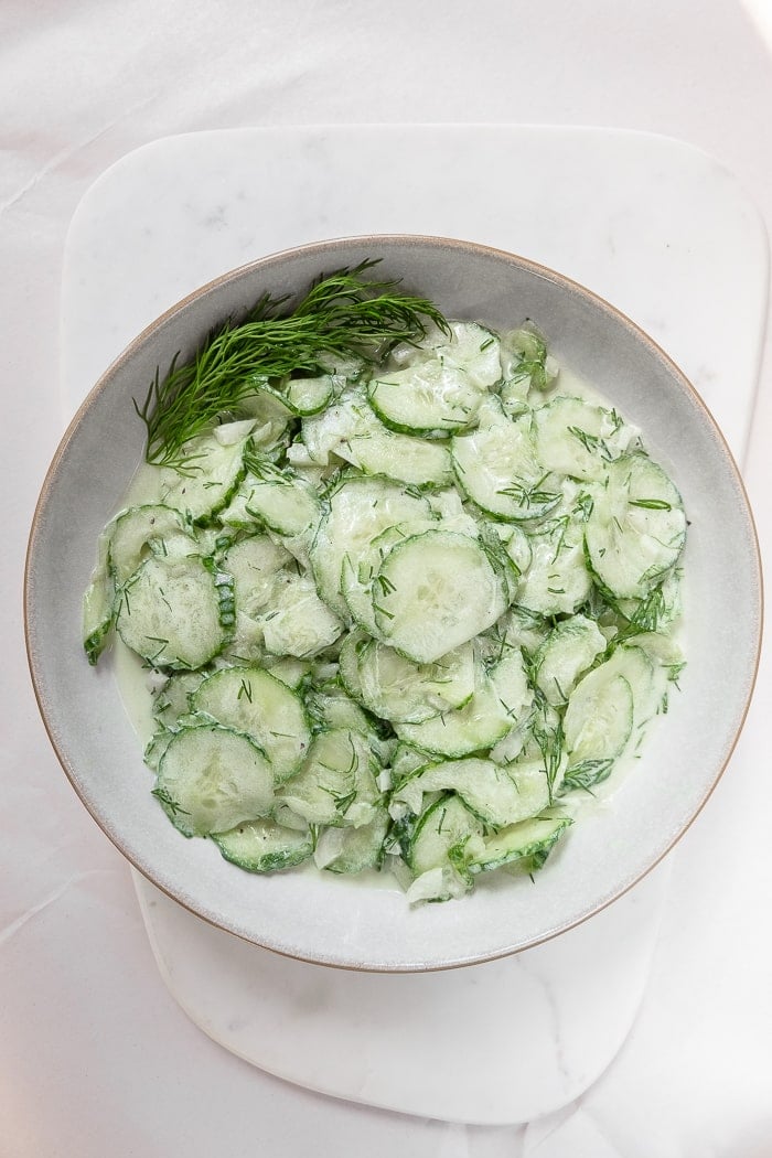 bowl of green german cucumber salad with dill on white marble