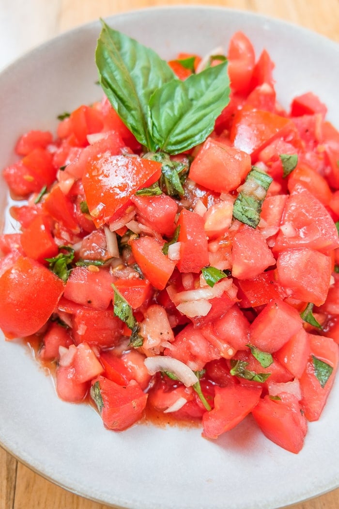 red tomatoes cut up with green basil in bowl