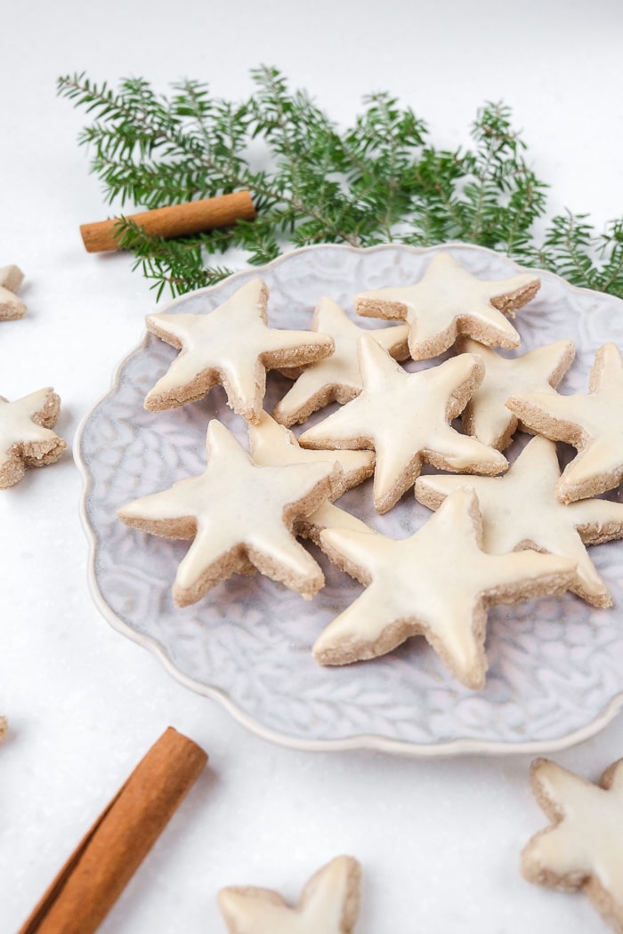 cinnamon star cookies on a plate with green branch behind