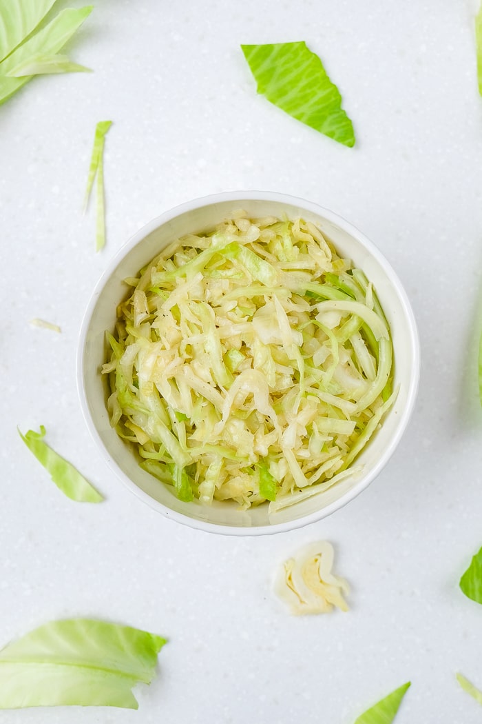 round white bowl of german coleslaw with shredded cabbage around