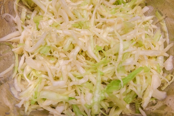 thin strips of green cabbage in metal mixing bowl