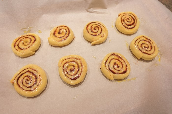 raw cinnamon rolls on parchment paper with egg wash