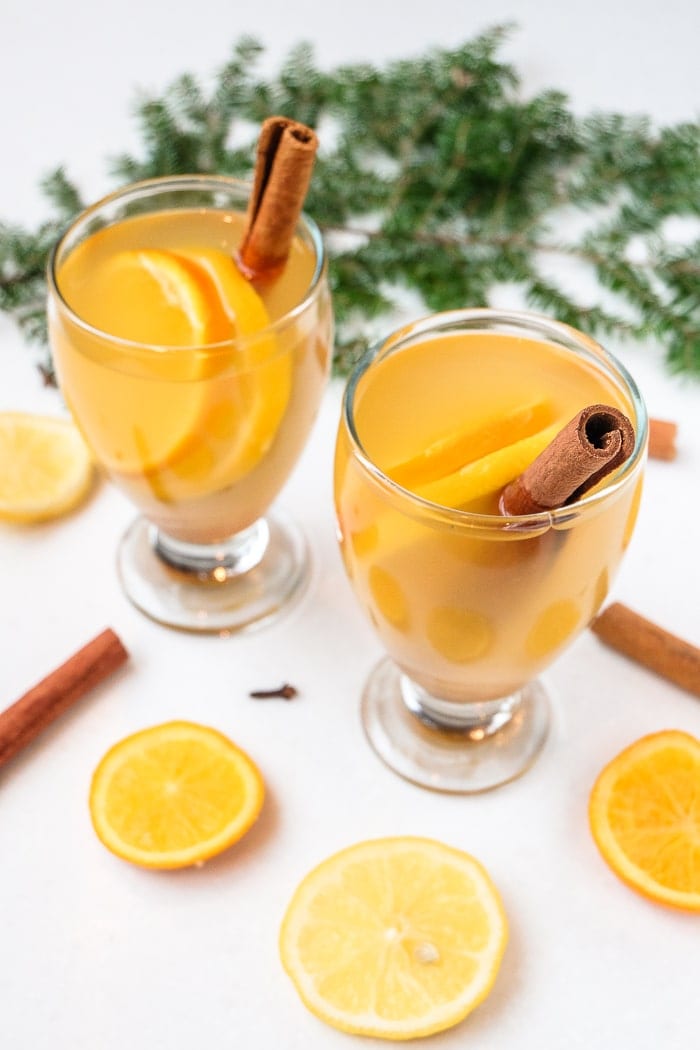 two glasses of mulled white wine on white table with cinnamon