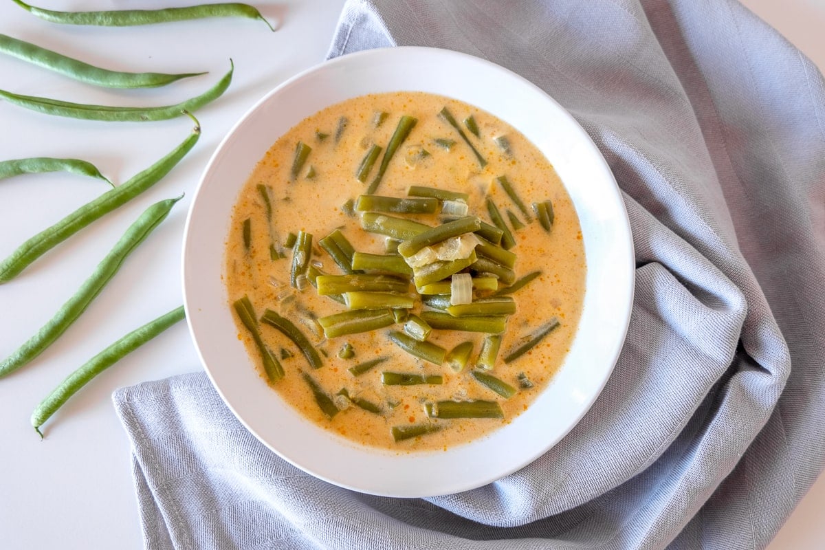 bowl of hungarian green bean soup with green beans and cloth beside