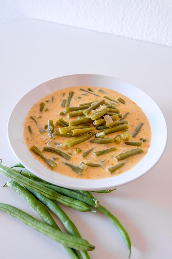 white bowl of orange bean soup on white table with green beans in front