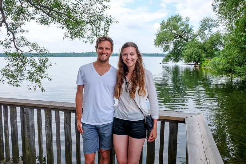 man and woman standing in front of a lake with green trees around
