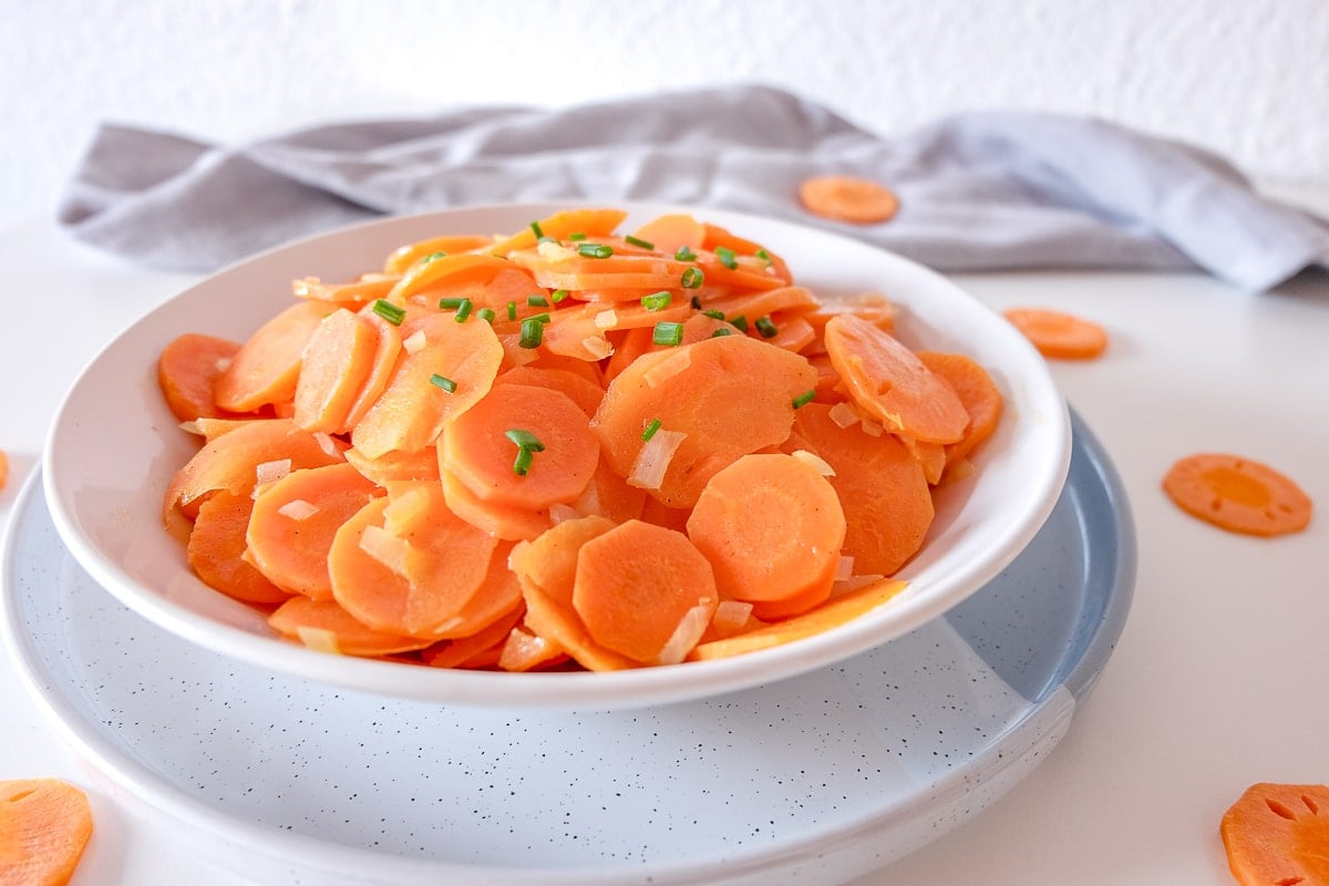 bowl of sliced carrot salad on white table with grey napkin behind