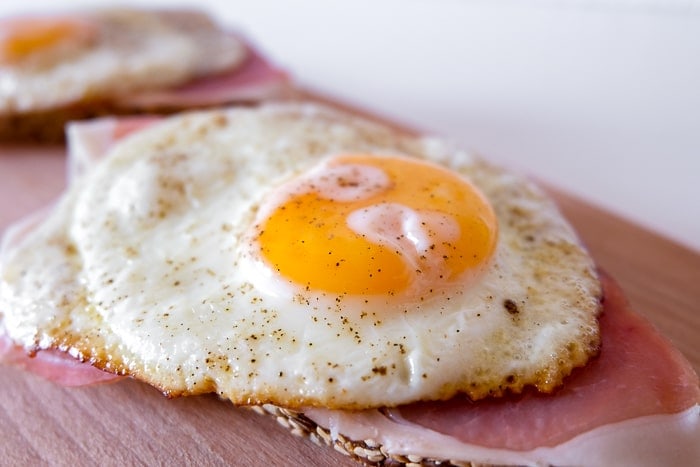 large fried egg with yolk on ham on cutting board