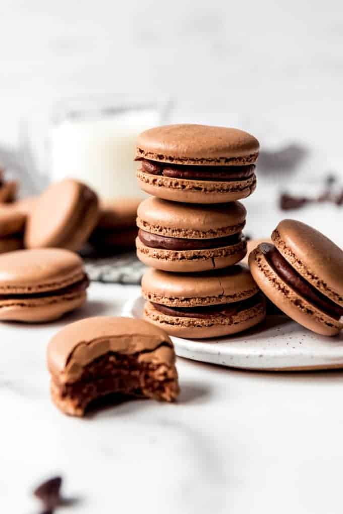 stack of chocolate macarons with half bitten macaron in front on white surface.