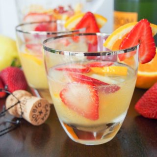 yellow sangria with cut up strawberries in glasses.
