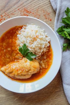 white bowl of easy chicken paprikash on wooden table with parsley