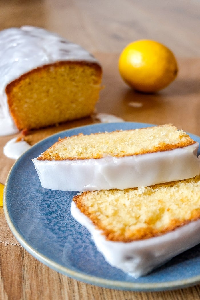 slices of yellow cake with white icing on blue plate with cake and whole lemon behind