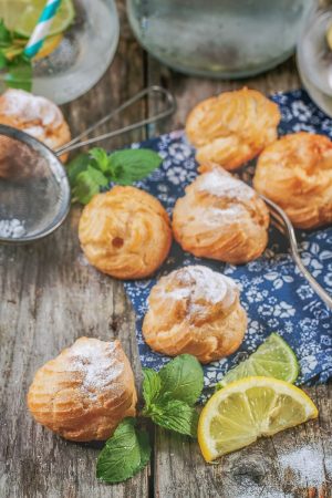 yellow cream puffs pastries on wooden table with lemon slice beside