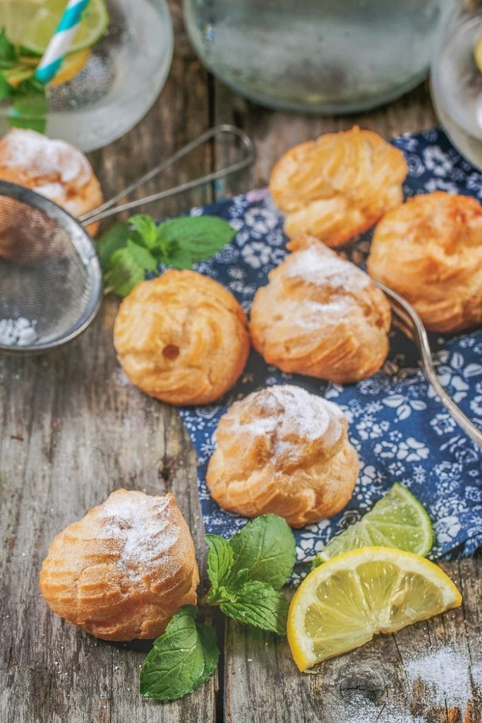 yellow cream puffs pastries on wooden table with lemon slice beside