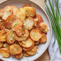 grey plate with fried potatoes beside green chives on cloth