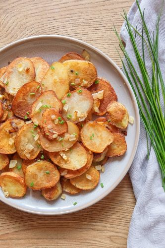 grey plate with fried potatoes beside green chives on cloth