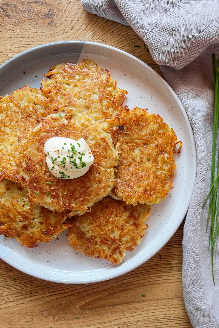 stack of potato pancakes on white plate with cloth and chives beside