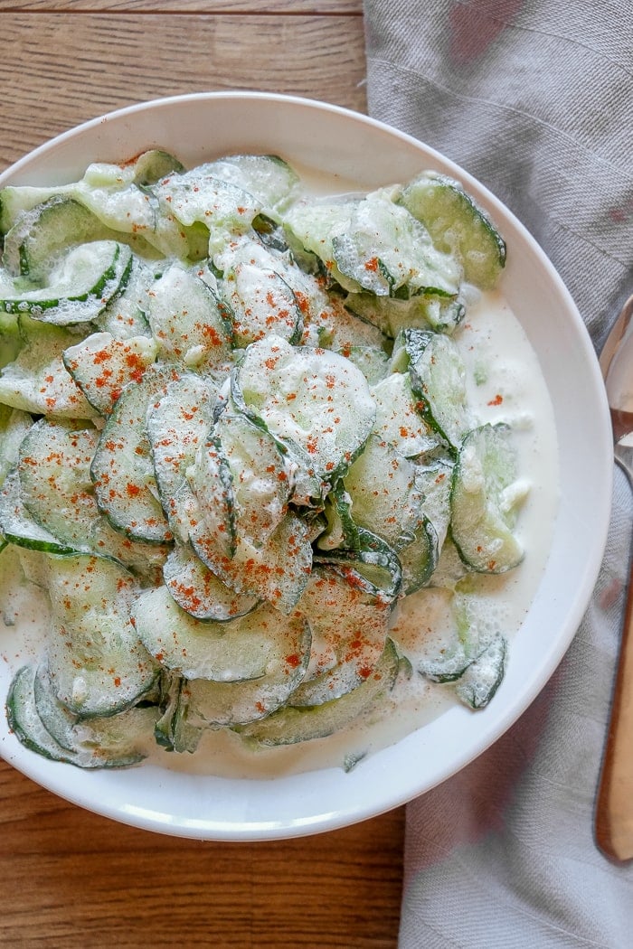 cucumber salad on white bowl with napkin beside on table