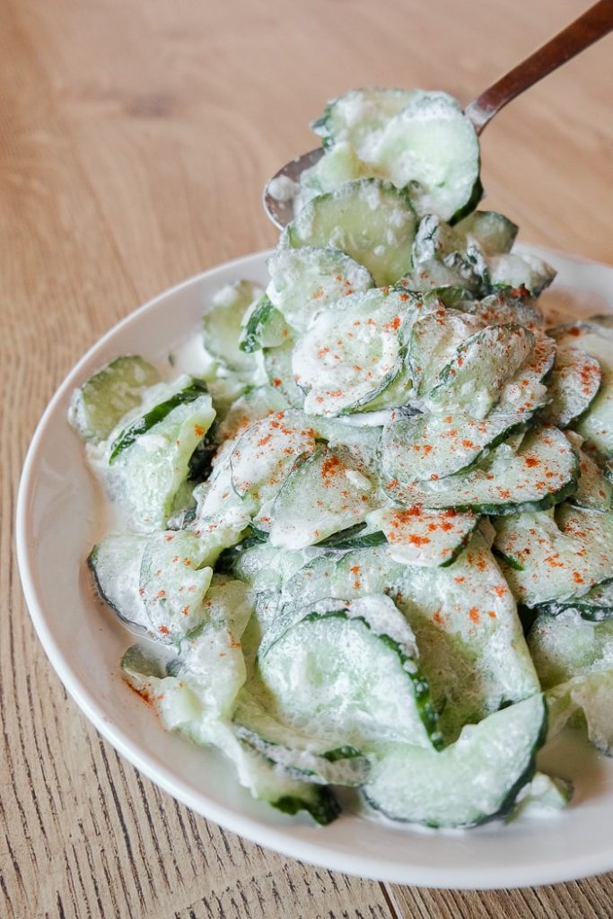 green hungarian cucumber salad in bowl with spoon scooping