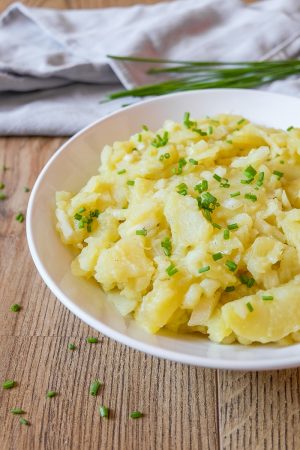 bowl of yellow potato salad with green chives behind