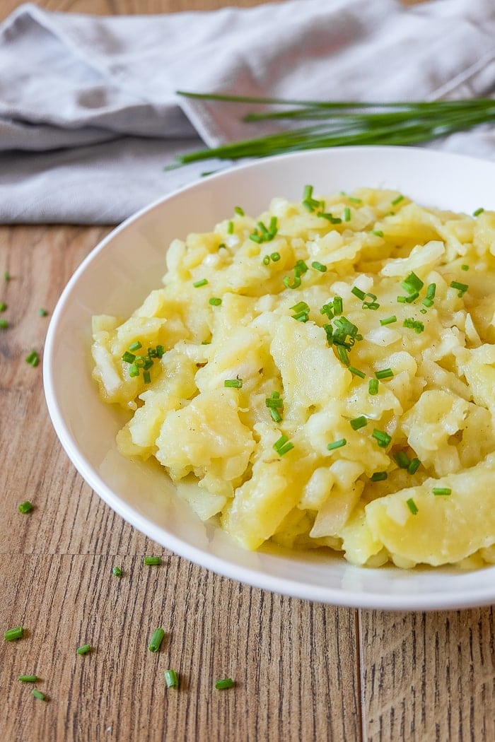 white bowl of potato salad with chopped chives around and on top