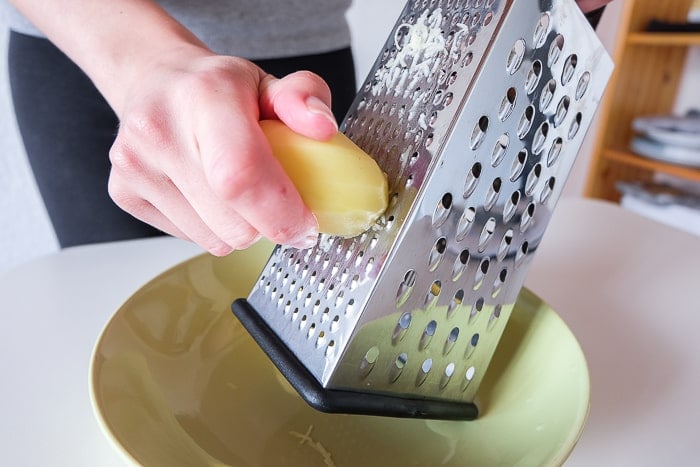 potato being grated on metal grater with hand