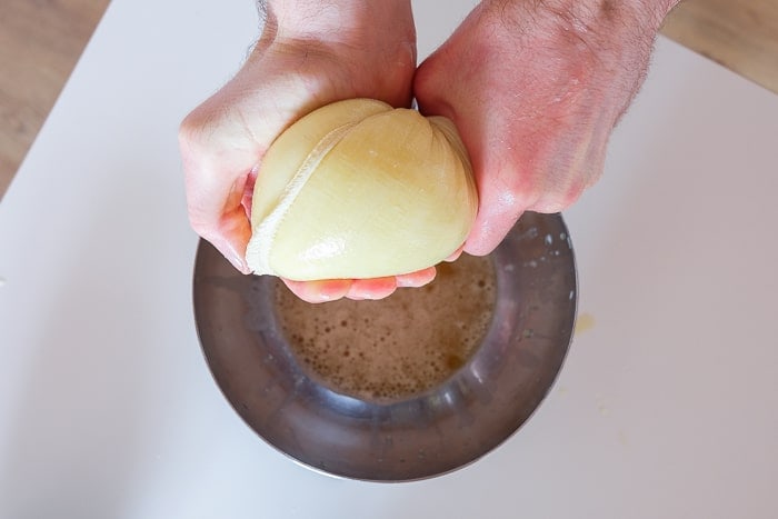 raw potatoes in cloth sack being squeezed over metal bowl