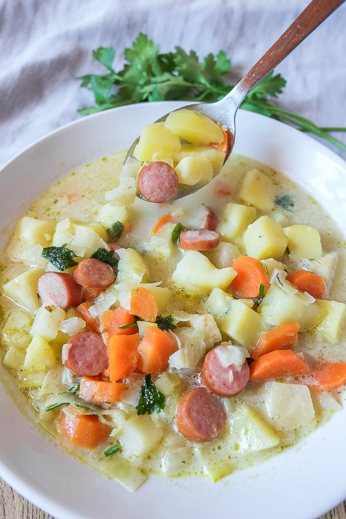 colourful vegetables in german potato soup with silver spoon in white bowl