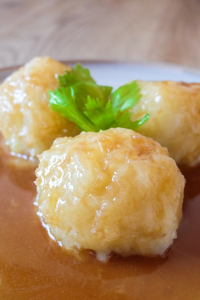 three potato dumplings on plate covered in gravy