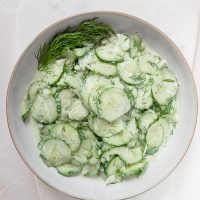 bowl of green german cucumber salad with dill on white marble