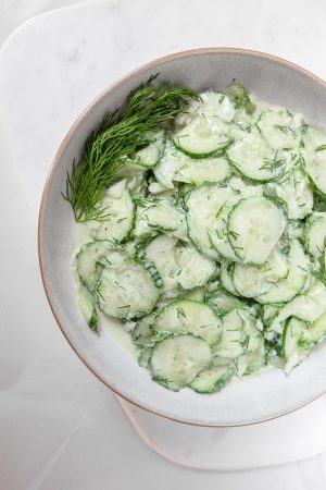 sliced cucumbers in german salad in bowl with dill on white marble
