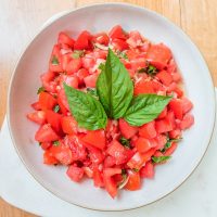 german tomato salad in bowl with basil on white marble