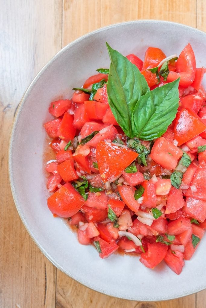 red tomato salad cut in bowl with basil sitting on wood