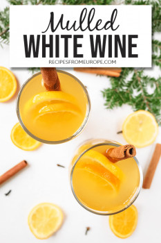 Photo of mulled white wine in glass with cinnamon stick and orange slices plus text overlay saying mulled white wine