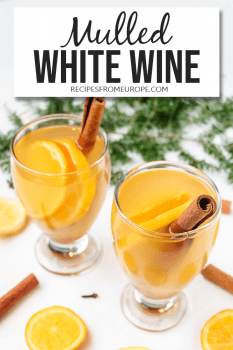 Photo of mulled white wine in glass with orange slices and cinnamon sticks around and text overlay saying mulled white wine