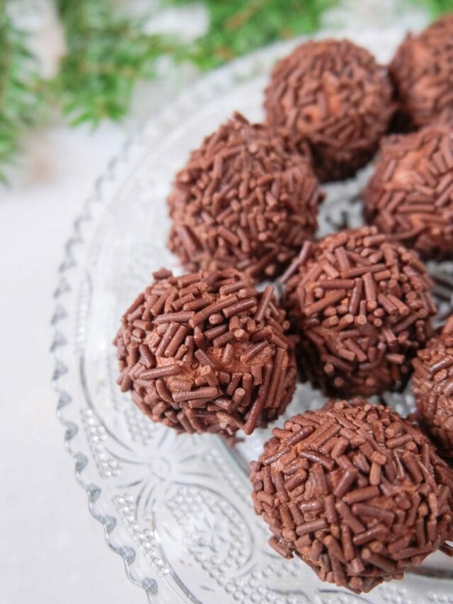 brown sprinkled german rum balls on clear plate with green branch behind