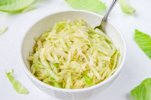 green german coleslaw in bowl with spoon and green cabbage around