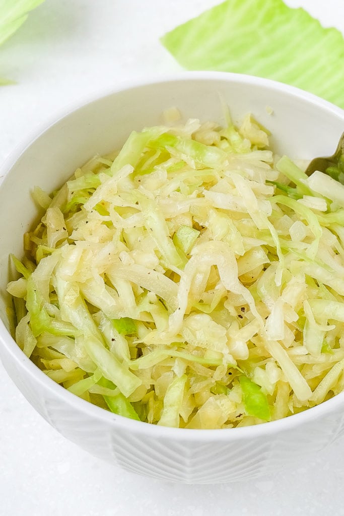 white bowl of green german coleslaw with cabbage leaves behind