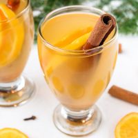 glass of mulled white wine with oranges and cinnamon sticks around
