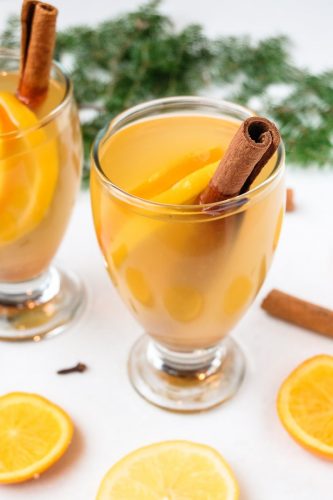 glass of mulled white wine with oranges and cinnamon sticks around