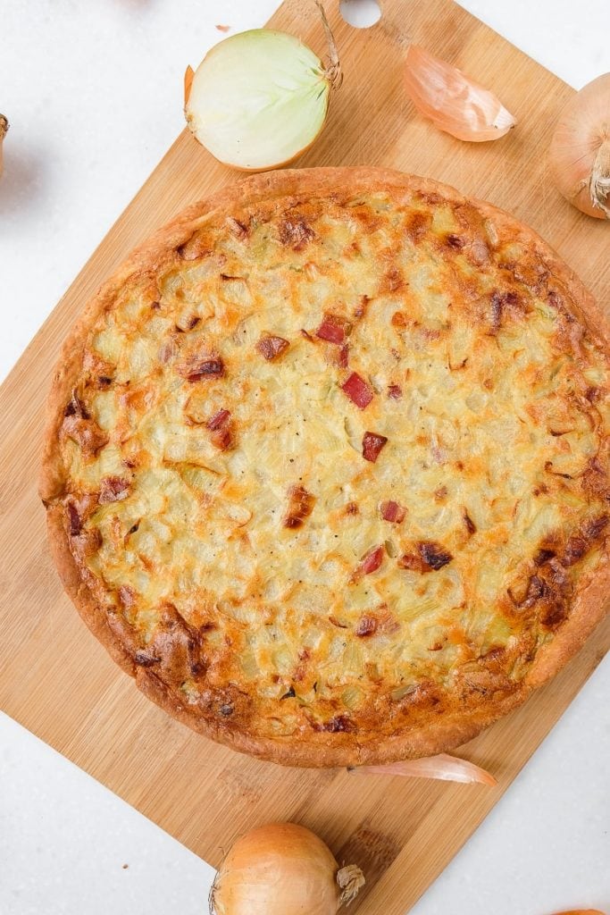 round german onion pie on wooden cutting board with onions around
