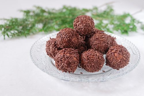 stack of german rum balls on clear plate on white counter with green branch behind.
