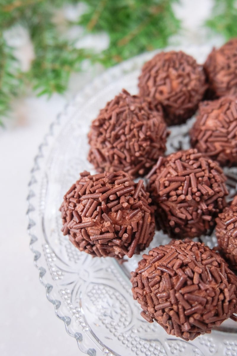 brown sprinkled german rum balls on clear plate with green branch behind.