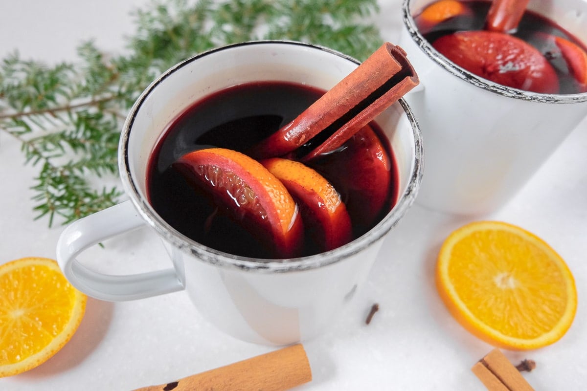 two mugs of hot red wine with orange slices and cinnamon sticks sticking out