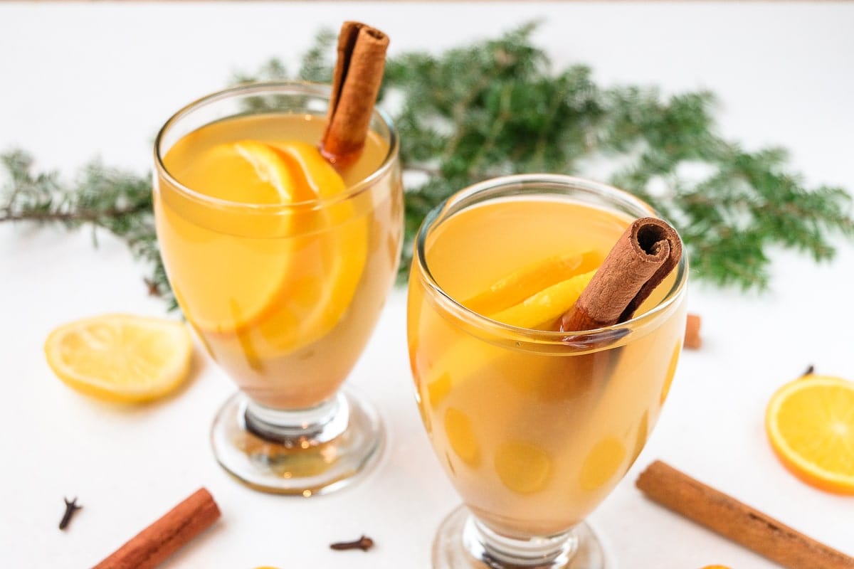 two glasses of mulled white wine with cinnamon sticks around
