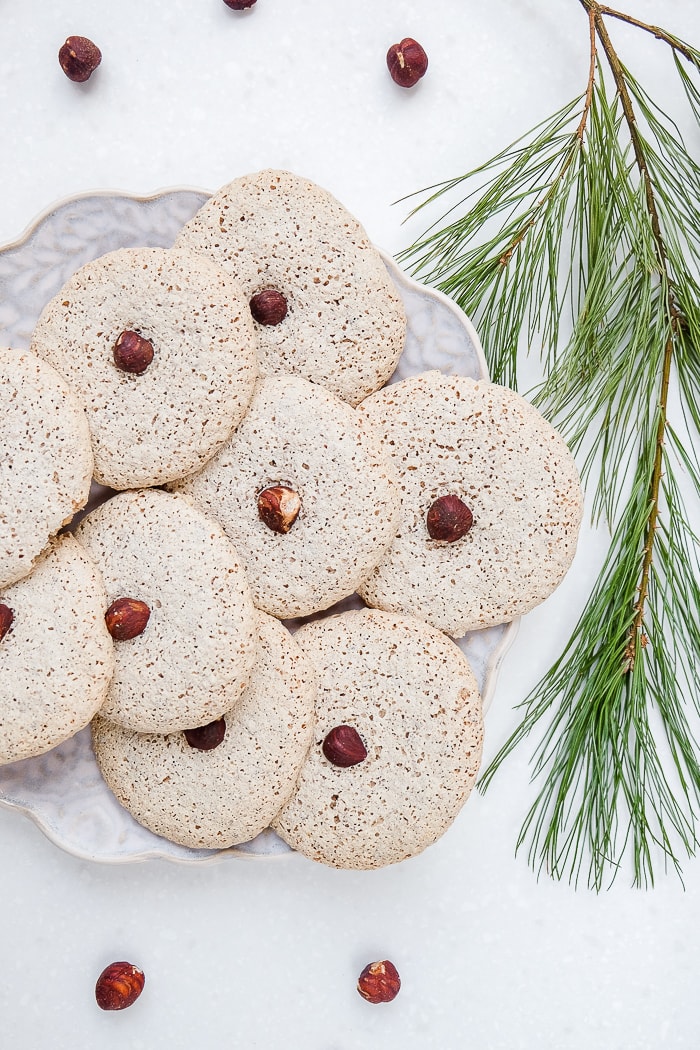 round hazelnut cookies with nuts in the middle on plate with branch beside
