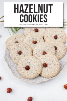 Photo of hazelnut cookies on purple plate and hazelnuts around it with text overlay saying hazelnut cookies